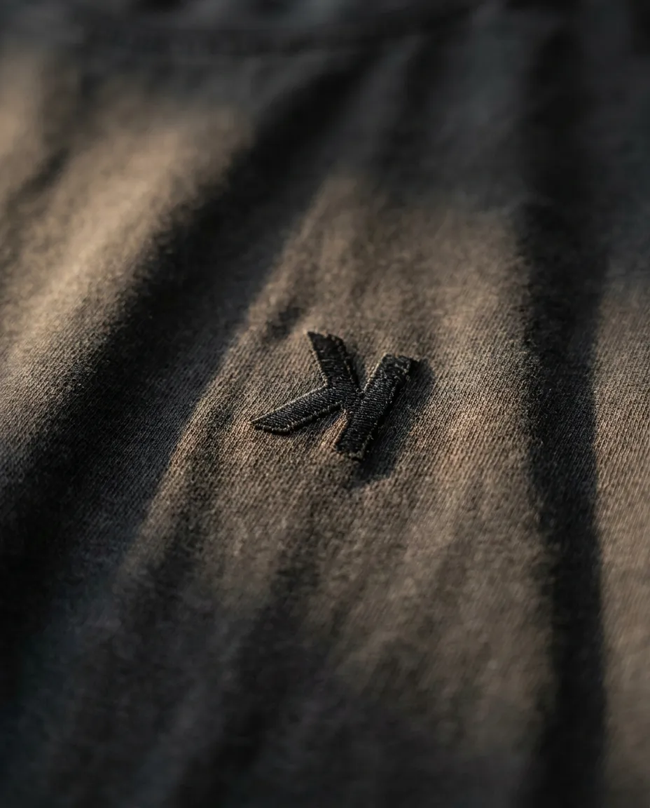 Macro of the tonal black-on-black embroidered k on the chest, in golden light